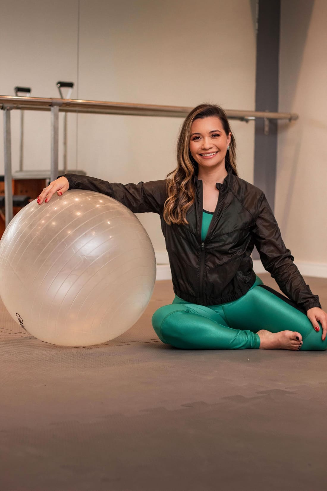 Ana sorrindo, sentada no estúdio ao lado de uma bola de pilates